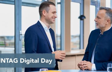 sonntag-header-events Two men in navy jackets converse in a bright modern office; a blue banner at the bottom reads 'SONNTAG Digital Day'.
